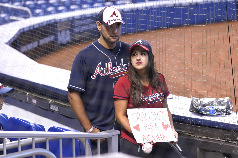 Khaled and Christine Taha hold a sign reading Prayers for Acuna as they wait to get autographs next to the Atlanta Braves dugout before a baseball game against the Miami Marlins, Sunday, July 11, 2021, in Miami. Atlanta Braves right fielder Ronald Acuna Jr. will undergo season-ending surgery after suffering a complete tear of the ACL in his right knee during Atlanta's 5-4 win over the Miami Marlins on Saturday. (AP Photo/Lynne Sladky)