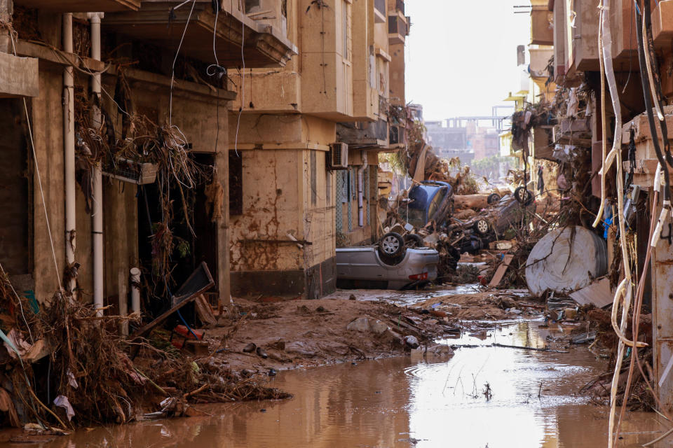 Overturned cars lie among other debris in a flooded street.