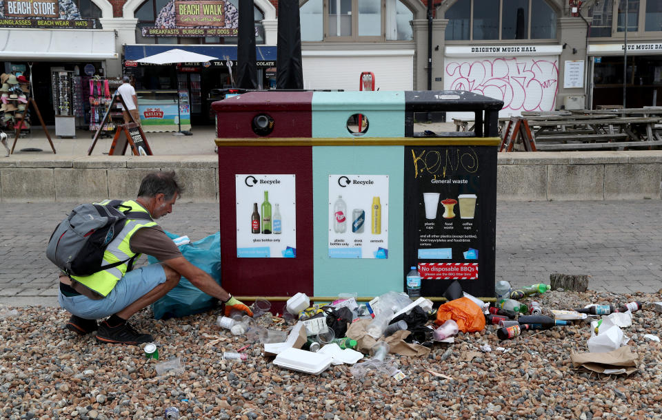 A man clears rubbish left by beachgoers in Brighton as thunderstorms and torrential rain are forecast to sweep across the UK, bringing an end to a week of blazing sunshine and scorching temperatures.