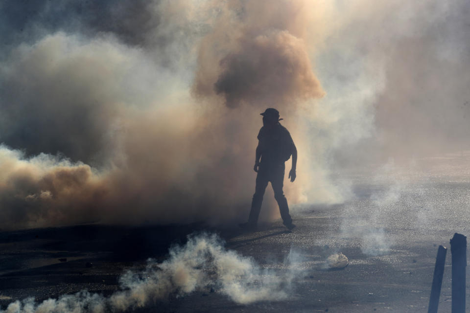 A protester stands amid tear gas fired by police trying to disperse an anti-government demonstration in Santiago, Chile, Friday, Dec. 27, 2019. Chile has been roiled by continuing and sometimes violent street protests since Oct. 18, when a student protest over a modest increase in subway fares turned into a much larger and broader movement with a long list of demands that largely focus on inequality. (AP Photo/Fernando Llano)