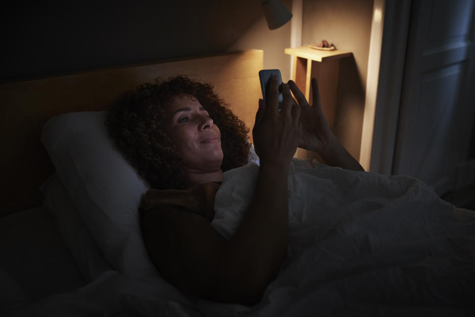 Smiling woman using smart phone while lying on bed