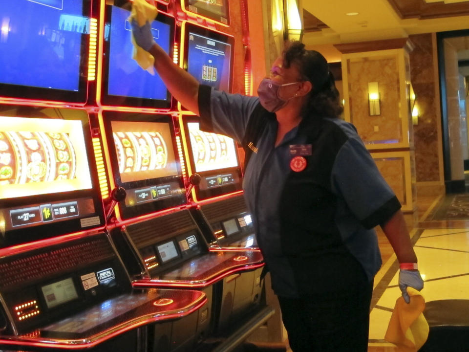 Jeorganna Barnes, a worker at Harrah's casino, on July 1, 2020, in Atlantic City, N.J., wipes slot machines with disinfectant as the casino prepared to reopen after 3 1/2 months of being shut down due to the coronavirus. On March 11, 2024, an independent report examining New Jersey's response to the pandemic said the state and nation were unprepared for it, adding the state is still underprepared for the next crisis. (AP Photo/Wayne Parry)