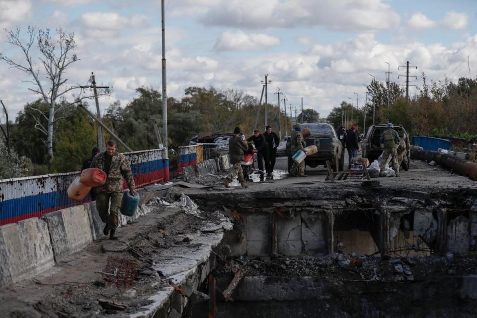 Ukrainian soldiers carrying supplies across a damaged bridge into the newly liberated city of Kupiansk, east of Kharkiv (EPA)