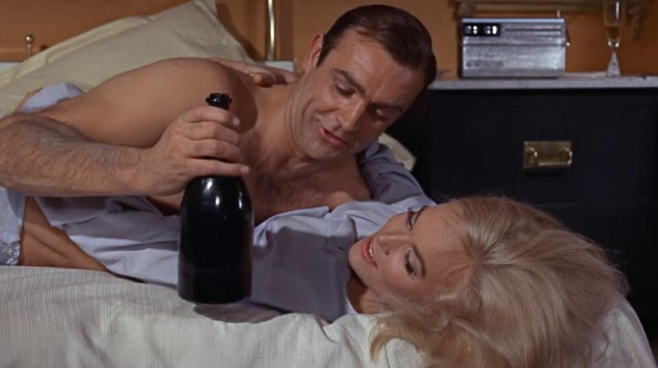 James Bond holding a bottle of champagne and lies on top of a woman
