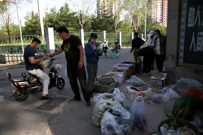 People buy vegetables and fruits at a street stall near a residential area in Beijing