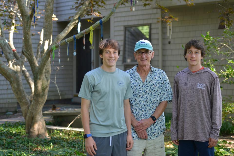 EAST FALMOUTH -- 09/21/23 -- Nathan Gartner, left, his twin brother, Silas Gartner, and their father, Ken Gartner, center, talk about running and the many races they have participated in including the Falmouth Road Race. Running medals hang from the tree at their family home. 
Merrily Cassidy/Cape Cod Times