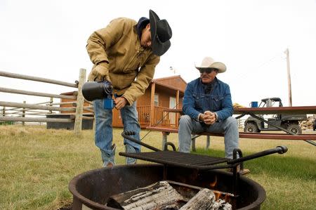 Jesse Bear (L) and his father, Sonny James Bear, a Three Affiliated Tribes member, drink coffee over the campfire during a break from training horses on their ranch just off the Fort Berthold Reservation in North Dakota, November 1, 2014. REUTERS/Andrew Cullen