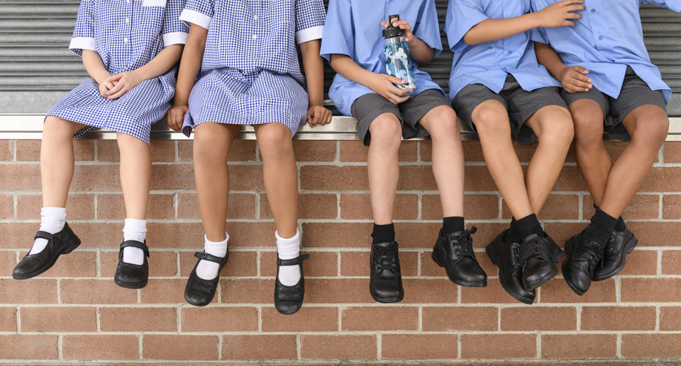 Five school children sitting on brick wall wearing school uniform.