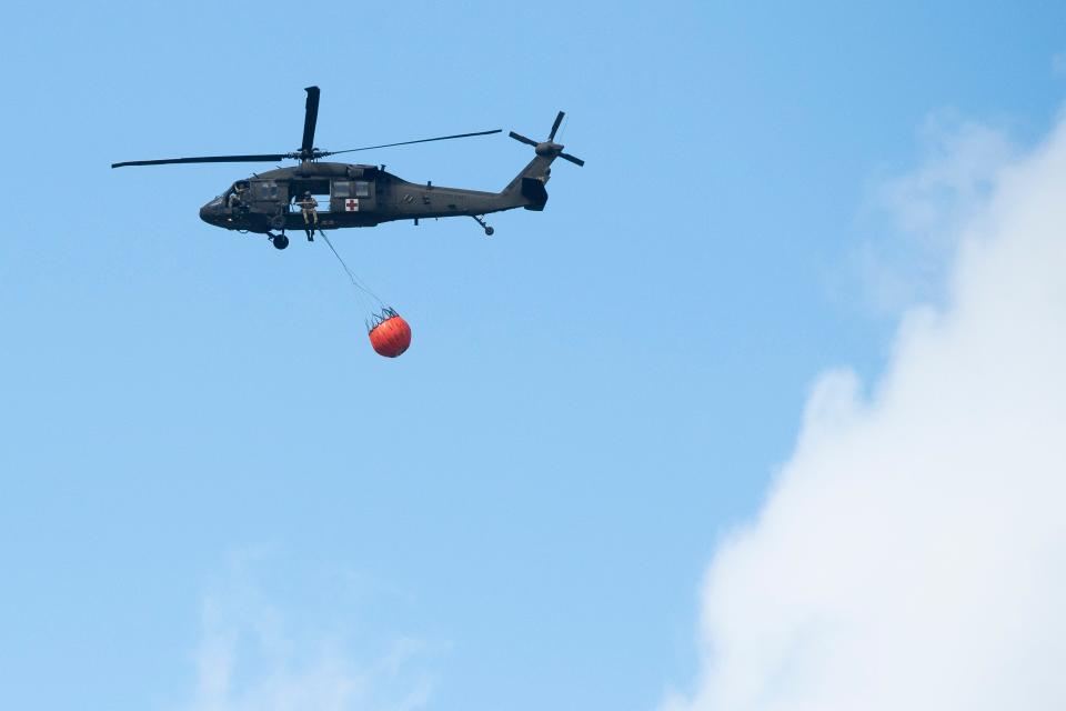 A helicopter flies over Wears Valley after dropping water in efforts to contain the Hatcher Mountain/Indigo Lane fire in Sevier County on Thursday, March 31, 2022.