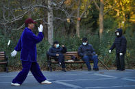 People wearing face masks to help curb the spread of the coronavirus chat each other as a man performs morning exercise at a park in Beijing, Monday, Nov. 23, 2020. (AP Photo/Andy Wong)