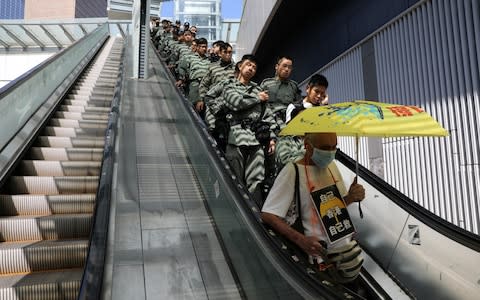 A line of police officers ride an escalator behind a protester holding an umbrella - Credit: AMMAR AWAD/REUTERS