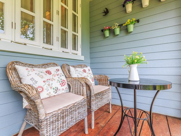 two wicker chairs with floral cushions in front of a coffee table on a porch with blue walls and wood floors