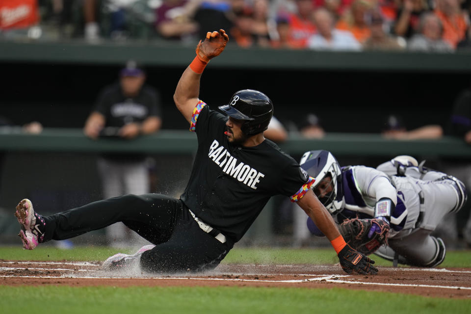 Baltimore Orioles' Anthony Santander, left, scores in front of Colorado Rockies catcher Elias Diaz on a sacrifice fly ball by Gunnar Henderson during the first inning of a baseball game, Friday, Aug. 25, 2023, in Baltimore. (AP Photo/Julio Cortez)