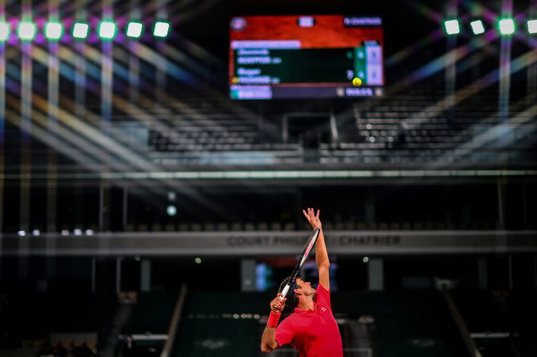 Iluminado pero desolado, el estadio Philippe Chatrier es testigo de un saque de Federer en una sesión sin público a raíz del toque de queda que rige a la noche en París.