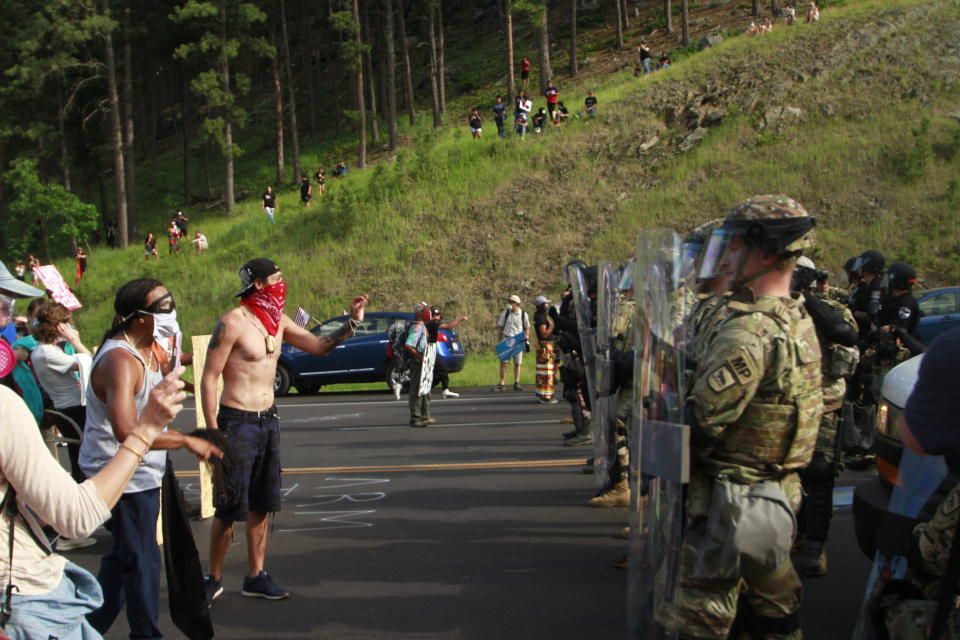 Protesters clash with a line of law enforcement officers in Keystone, S.D., on the road leading to Mount Rushmore ahead of President Donald Trump's visit to the memorial on Friday, July 3, 2020. (AP Photo/Stephen Groves)