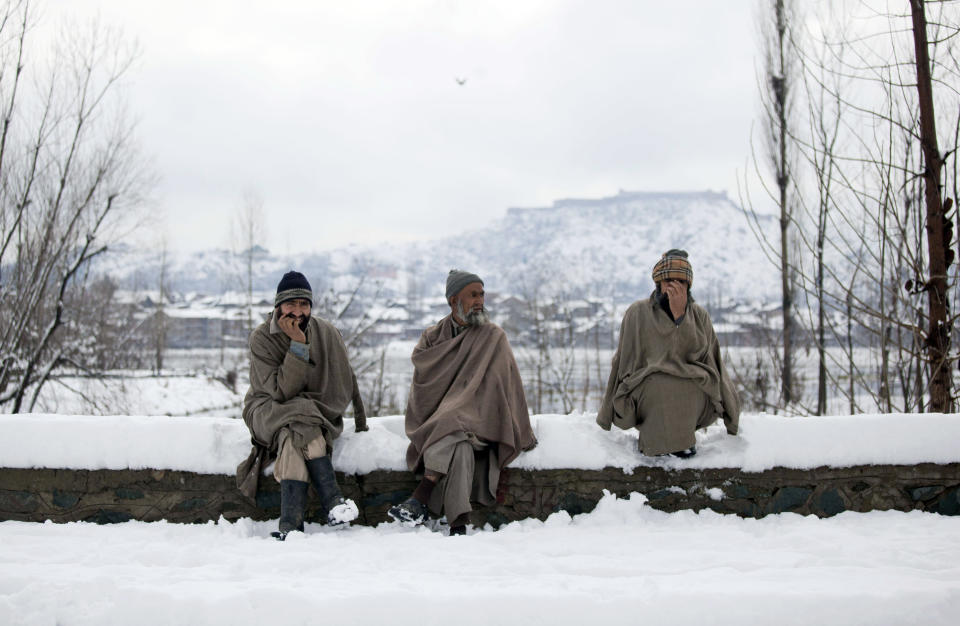 Kashmiris wait for transport on a snow covered road on the outskirts of Srinagar, India, Wednesday, March 12, 2014. Unusually heavy snowfall has unleashed avalanches and collapsed homes in the Himalayan region of Kashmir, killing at least 14 people on both sides of the de-facto border between India and Pakistan, officials said. (AP Photo/Dar Yasin)