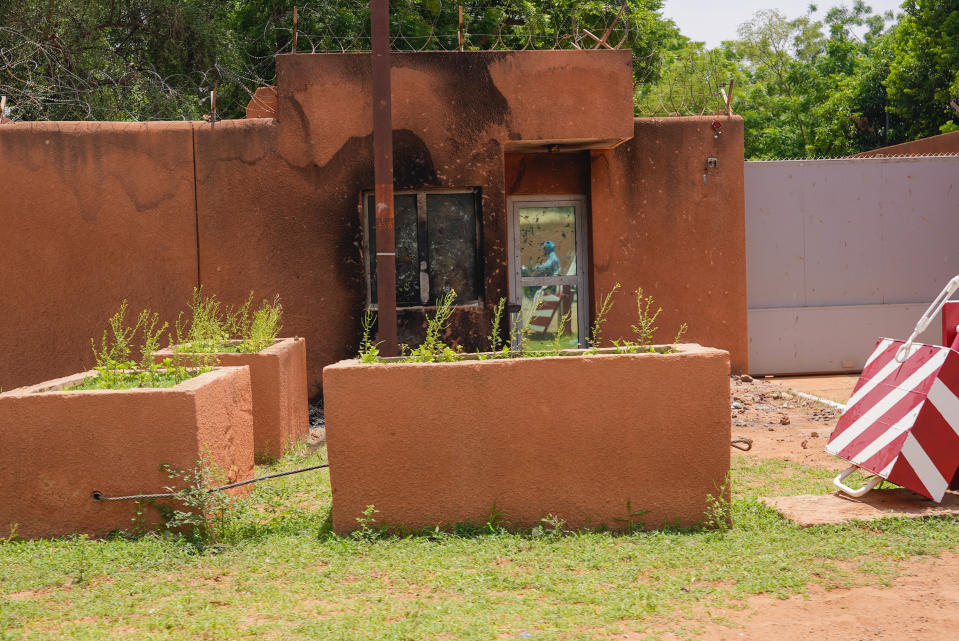 A motorcyclist is reflected in the shattered door of the French embassy in Niamey, Niger, Monday, July 31, 2023, one day after supporters of coup leader Gen. Abdourahmane Tchiani burned the entrance of the embassy during anti-French protest. West African nations have given Niger's coup leaders one week to reinstate the country's democratically elected president and have threatened to use force if the demands aren't met. (AP Photo/Sam Mednick)