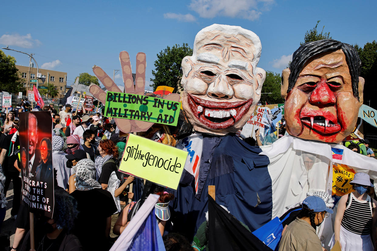 Demonstrators hold signs next to puppets of political figures.