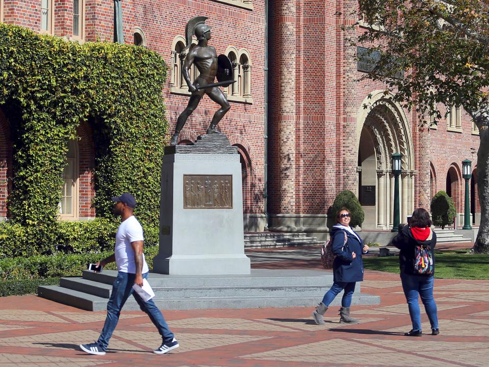 FILE - In this March 12, 2019 file photo, people pose for photos in front of the iconic Tommy Trojan statue on the campus of the University of Southern California in Los Angeles. USC will phase in free tuition for students from families with an annual income of $80,000 or less, USC President Carol L. Folt announced Thursday, Feb. 20, 2020. As part of the initiative, ownership of a home will not be counted in determining a student's financial need. (AP Photo/Reed Saxon, File)