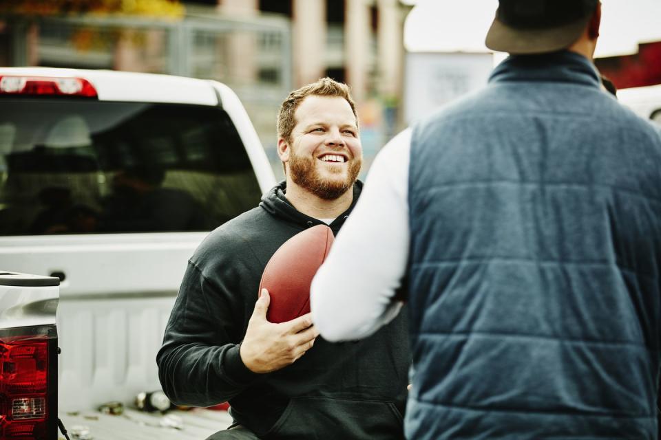 smiling man holding football hanging out with friend during tailgating party