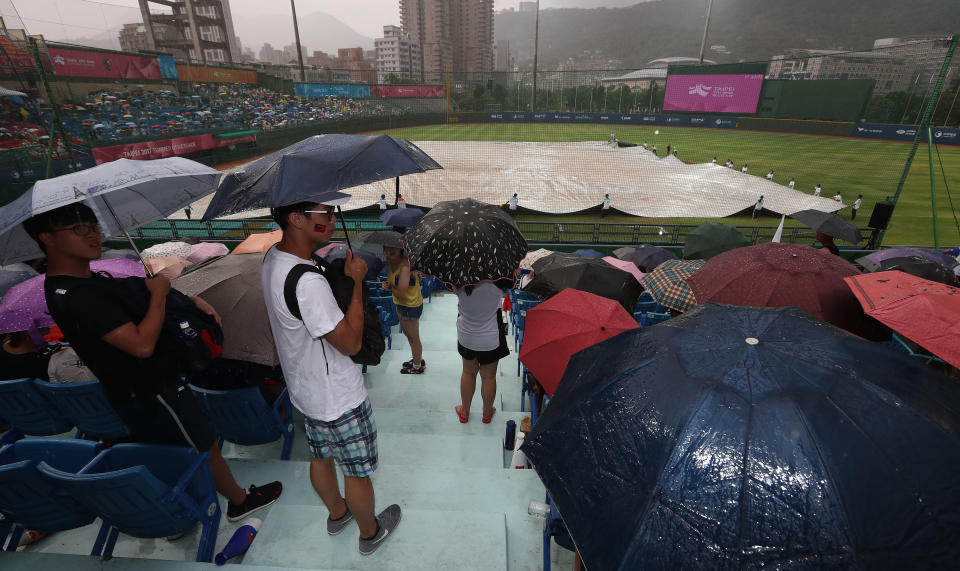 世大運棒球賽中華隊23日原訂晚間6時30分與南韓隊在天母球場交手，這場比賽攸關中華隊能否晉級4強。賽前天母球場下起雨，主辦單位在內野拉起帆布，先宣布延後開打，許多球迷也在場邊撐起雨傘，等待比賽開始。(中央社)