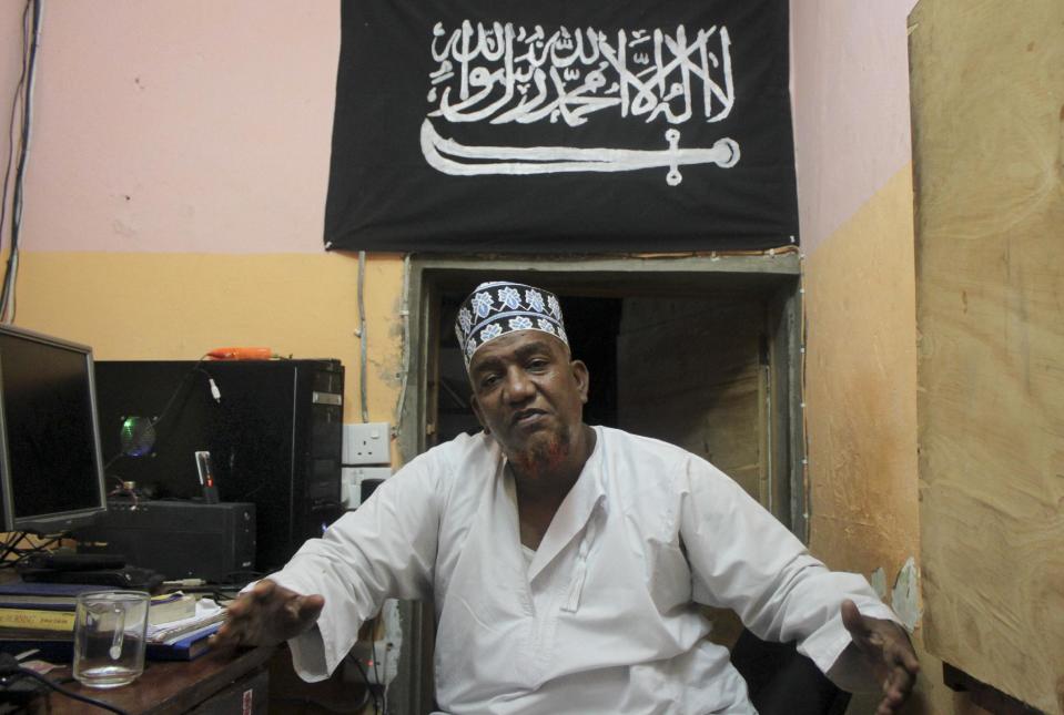 FILE - In this Tuesday Oct. 29, 2013 file photo, Abubakar Shariff Ahmed, an influential member of a controversial mosque where two previous mosque leaders were killed under mysterious circumstances, sits in his office in Mombasa, Kenya. Writing in Arabic on Islam flag reads: "There is no God but God and Muhammed is his messenger". The lawyer for radical Islamic leader Abubakar Shariff Ahmed, who had been sanctioned by the United States and the United Nations for supporting the al-Qaida-linked Somali militant group al-Shabab, says his client has been assassinated Tuesday, April 1, 2014 along with another man whose identity has not yet been established, near the Shimo la Tewa prison in Mombasa, Kenya. (AP Photo/Jason Straziuso, File)