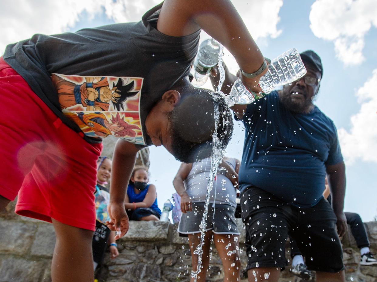 Jaizir Remillard, 10, pours water on himself after early dismissal at City View Discovery School Thursday. Nate Bowens, parent of another student, adds more water.