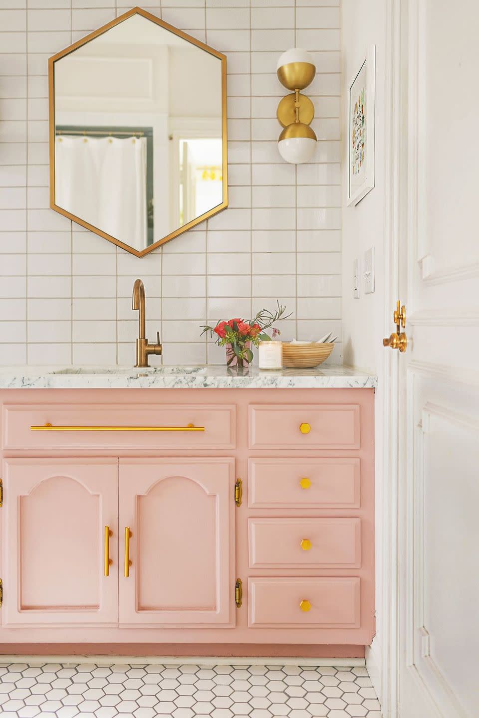<p>Gold, white and soft pink make an elegant combination. This bathroom's white tiles and gold fixtures pair well with the pink dresser and window's light. </p>