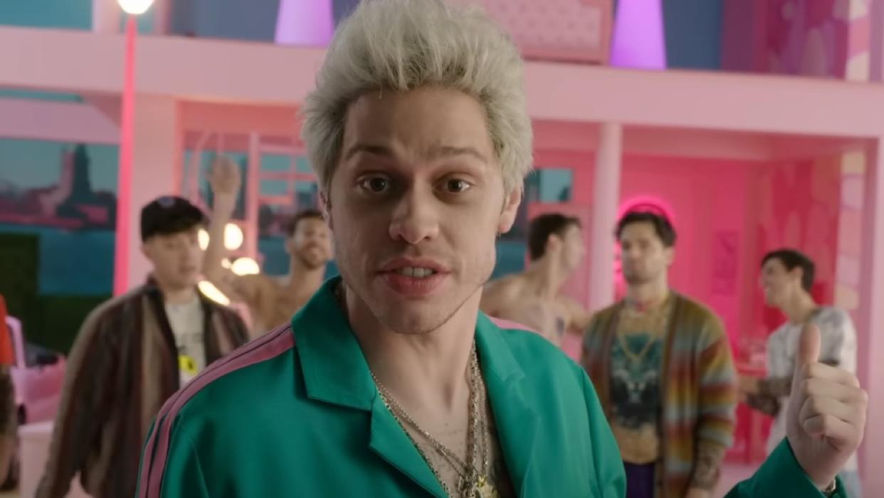  A screenshot of Pete Davidson pointing behind him at a Barbie set. 