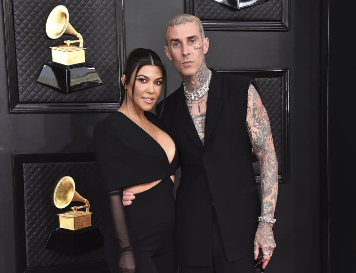 A heavily tattooed man puts his arm around the waist of a woman in a black gown