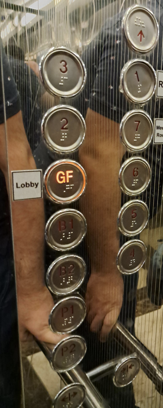 Elevator panel showing floors 1 to 7, B1 to B3, with the ground floor (GF) button lit. Person's arm reflected in the panel