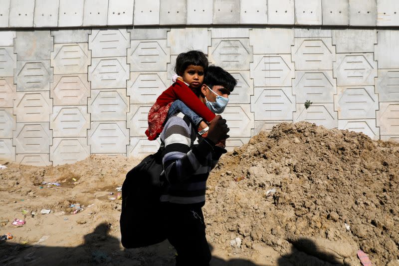 A migrant worker carries his daughter as they walk to their bus to return to their village, during a 21-day nationwide lockdown to limit the spreading of coronavirus disease (COVID-19), in Ghaziabad