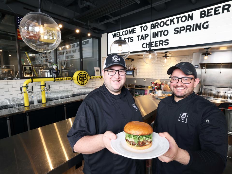 Brockton Beer Company co-head chefs from left, Markos Liapopoulos and Christos Liapopoulos, with a BBC Burger topped with BBC bourbon bacon jam, brie cheese, pickles and arugula on Wednesday, May 1, 2024.