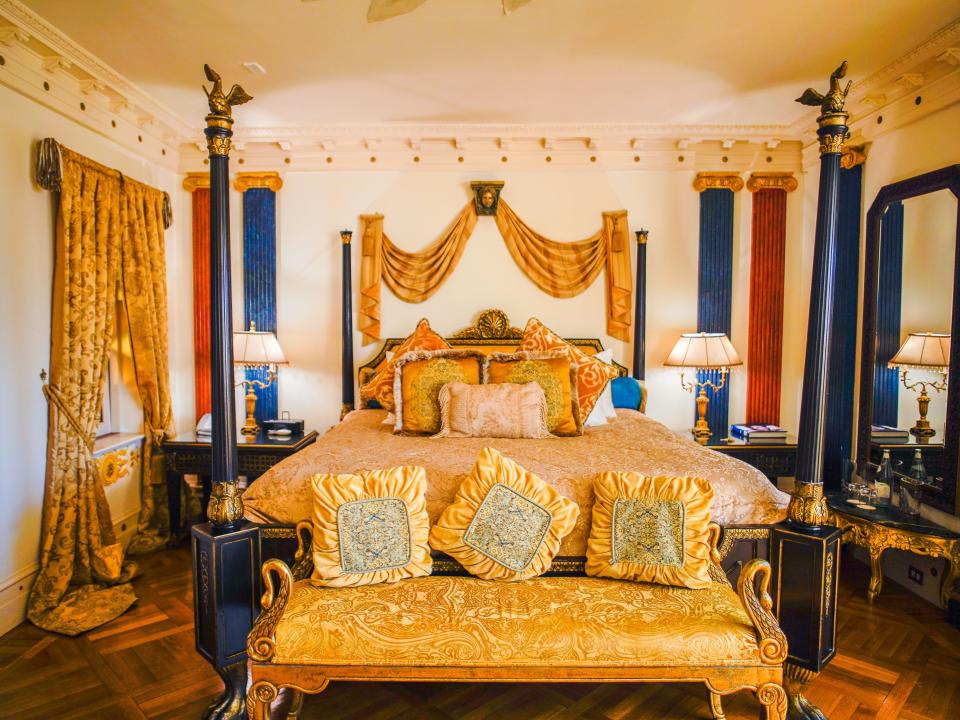 A wide shot of the Aurora Suite in the former Versace Mansion shows the golden bed with lamps on either side