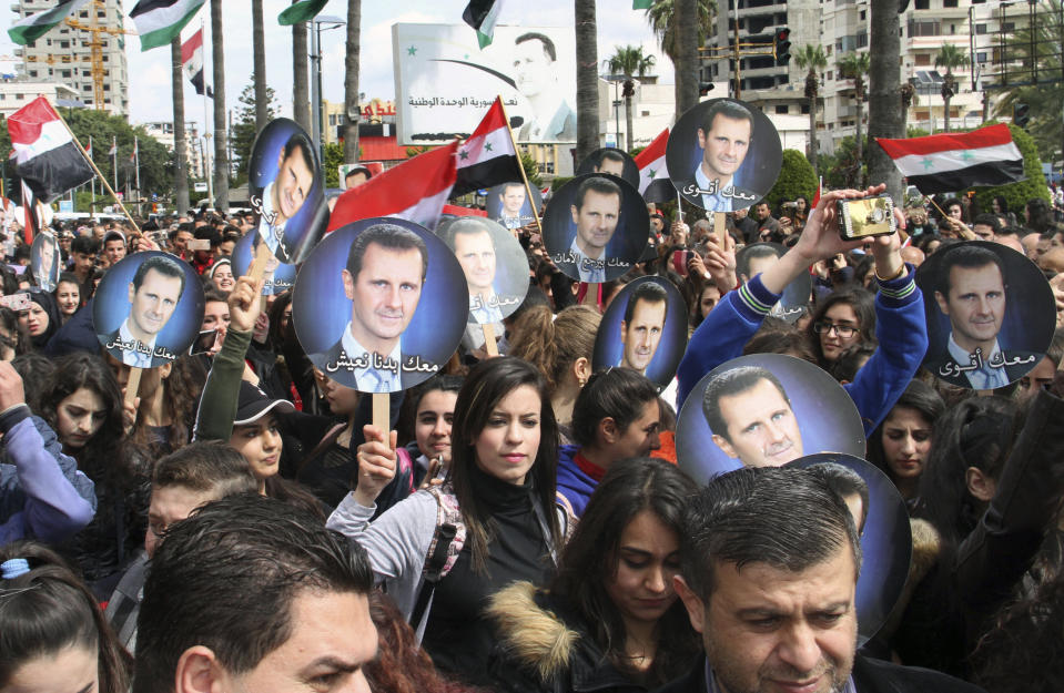 FILE - In this March. 27, 2019, file photo released by the Syrian official news agency SANA, people hold Syrian flags and portraits of President Bashar Assad during a protest against U.S. President Donald Trump's move to recognize Israeli sovereignty over the Israeli occupied Golan Heights, in the costal port city of Tartus, Syria. Assad has snapped up a prize from world powers that have been maneuvering in his country’s multifront wars. Without firing a shot, his forces are returning to towns and villages in northeastern Syria where they haven’t set foot for years. (SANA via AP, File)