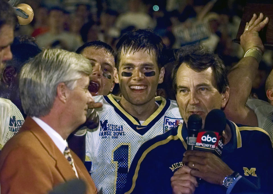 FILE - Michigan quarterback Tom Brady, center, with coach Lloyd Carr, right, celebrate at the FedEx Orange Bowl NCAA college football game after a 35-34 overtime win against Alabama at Pro Player Stadium in Miami Gardens, Fla., Jan. 1, 2000. Tom Brady has retired after winning seven Super Bowls and setting numerous passing records in an unprecedented 22-year-career. He made the announcement, Tuesday, Feb. 1, 2022, in a long post on Instagram. (Daniel Mears/Detroit News via AP, File)