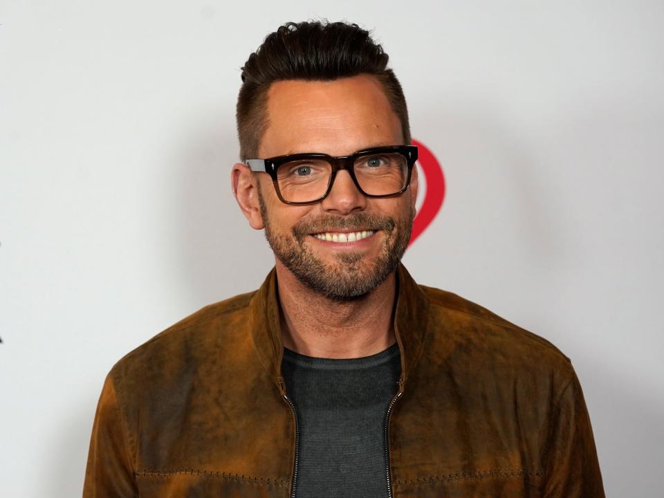 Joel McHale, wearing glasses, smiles at an event.