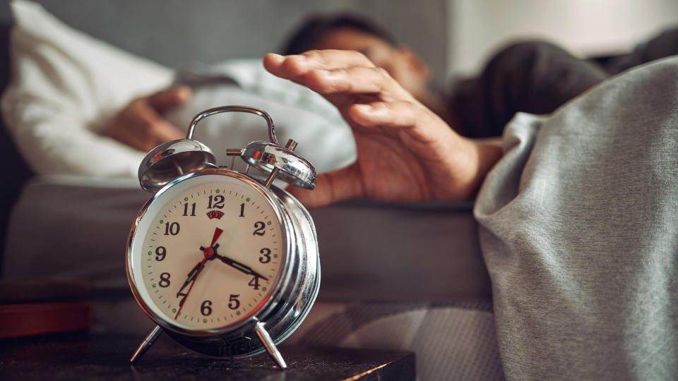 A person being woken up in the morning, reaching for the alarm clock