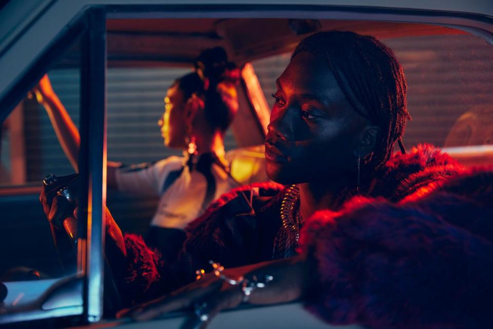 A close-up shot of two people in a car at night, bathed in a red and blue light.