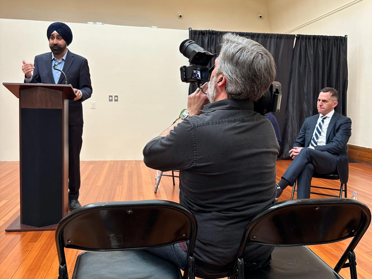 Menendez looks on as Bhalla's opening remarks at a Jersey City candidate forum are filmed by a cameraman.
