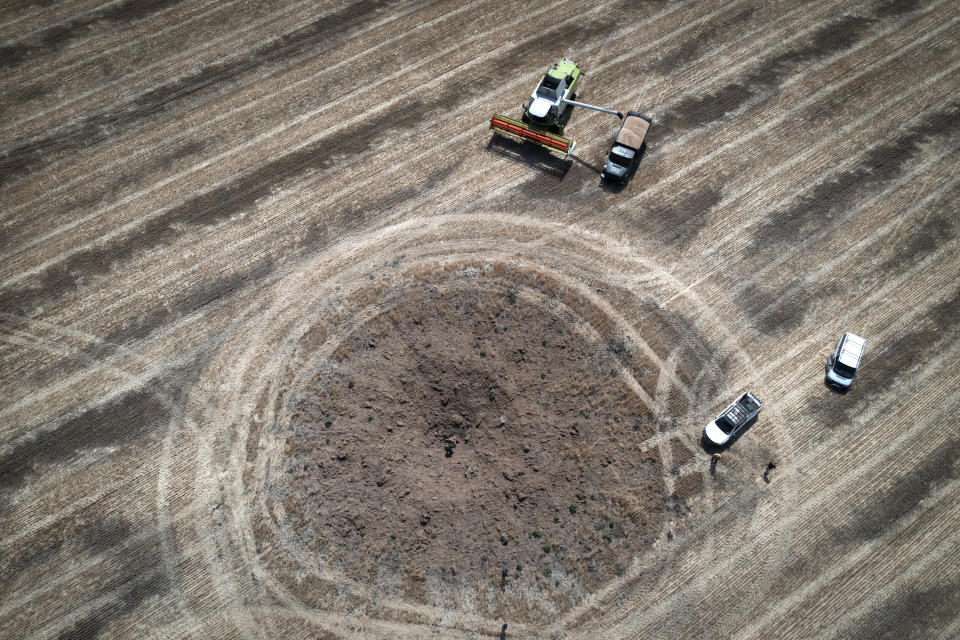 A farmer collects harvest on a field ten kilometres from the front line where fierce battle is going, a crater left by the Russian rocket in the foreground, in the Dnipropetrovsk region, Ukraine, Monday, July 4, 2022. An estimated 22 million tons of grain are blocked in Ukraine, and pressure is growing as the new harvest begins. The country usually delivers about 30% of its grain to Europe, 30% to North Africa and 40% to Asia. But with the ongoing Russian naval blockade of Ukrainian Black Sea ports, millions of tons of last year’s harvest still can’t reach their destinations. (AP Photo/Efrem Lukatsky)