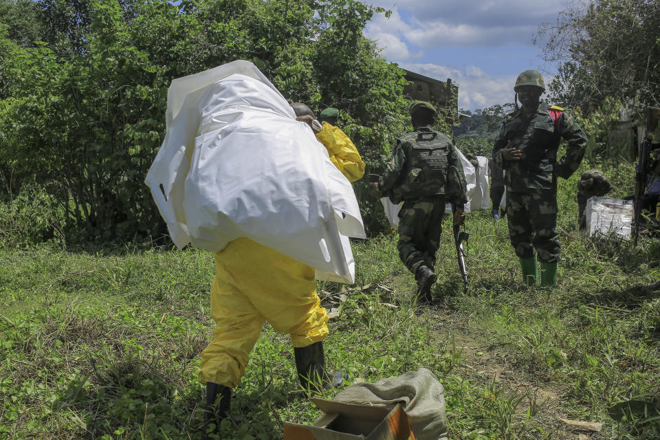 A Congolese soldier looks on as a forensics worker carries white plastic bags used to hold human remains discovered at a mass grave in the village of Ndoma, near Beni in North Kivu, Congo Saturday, May 6, 2023. The remains of at least 20 people were found buried in a mass grave in an area used to cultivate cacao in Ndoma village in Congo's North Kivu province this weekend, according to local authorities and a military spokesperson. (AP Photo)