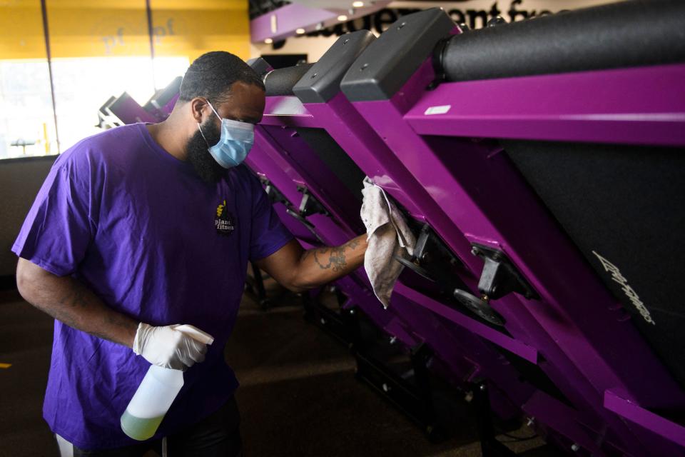 A man carrying a spray bottle and rag cleans fitness equipment.