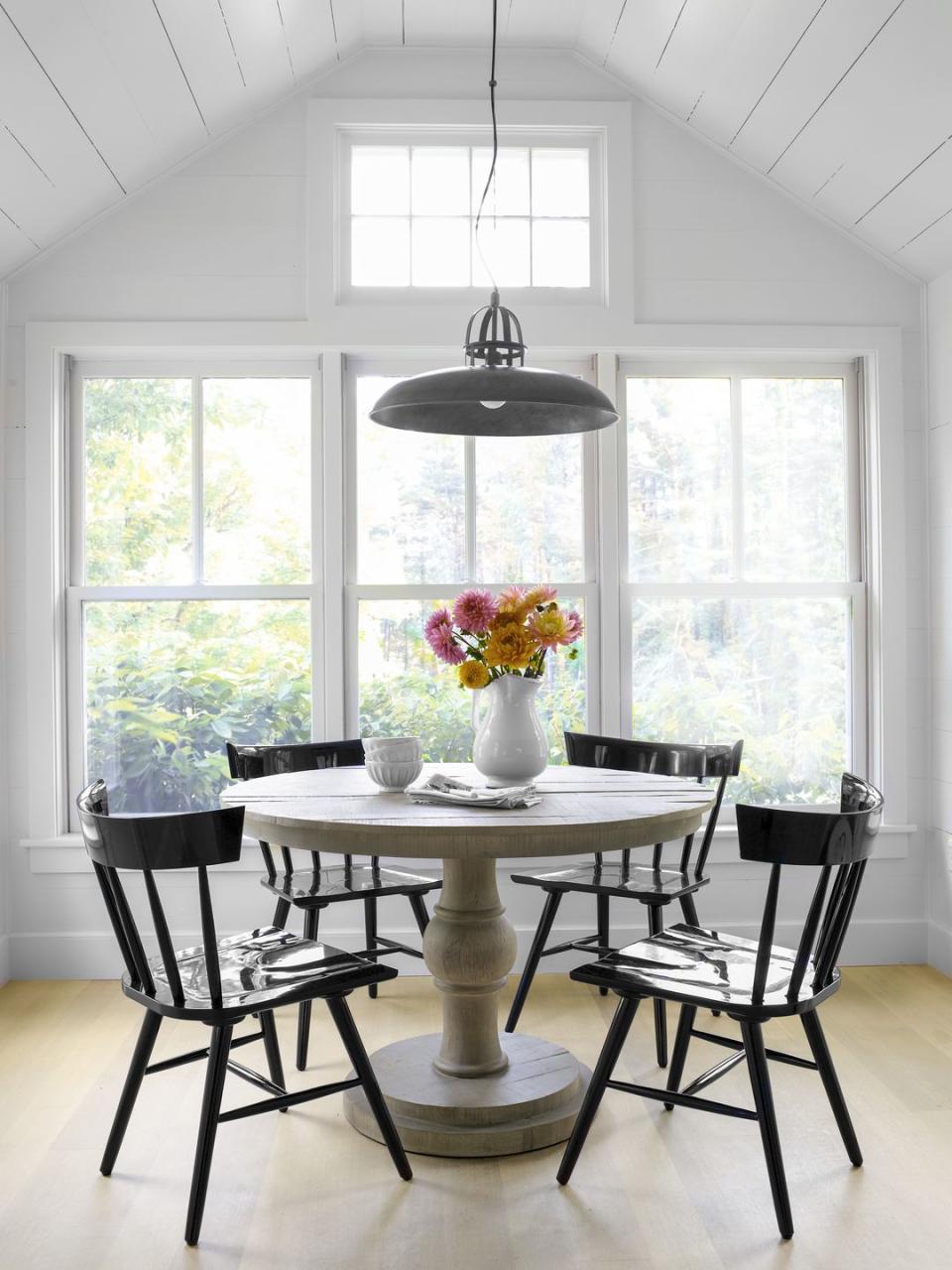 a round dining room table with black chairs and a vase of flowers