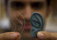 In this Monday, July 2, 2012 photo Tom Cervantes, of Boston, a research engineer at the Laboratory for Tissue Engineering and Organ Fabrication at Massachusetts General Hospital, displays a titanium frame designed for the reconstruction of a human ear, left, and a three dimensional plastic ear model, right, at the lab, in Boston. Scientists are growing ears, bone and skin in the lab, and doctors are planning more face transplants and other extreme plastic surgeries. Around the country, the most advanced medical tools that exist are now being deployed to help America's newest veterans and wounded troops. (AP Photo/Steven Senne)