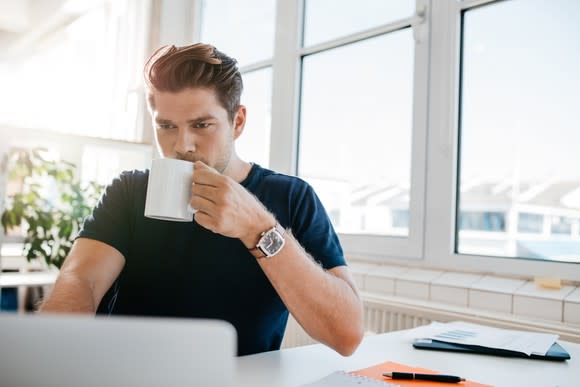 Young male adult at a laptop with mug in hand