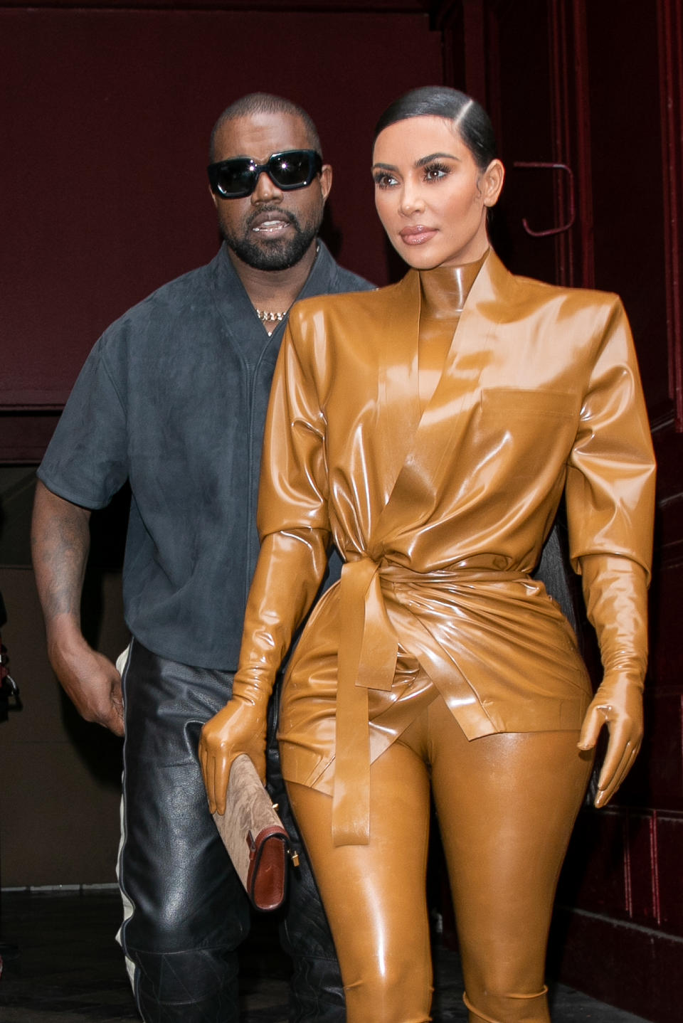 Kanye West and Kim Kardashian exiting a venue, Kim in a glossy metallic outfit with tied waist, Kanye in a grey shirt