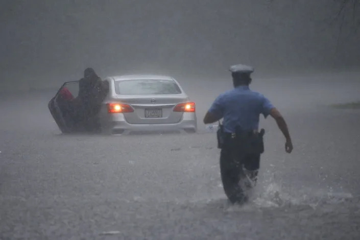 FILE - A Philadelphia police officer rushes to help a stranded motorist during Tropical Storm Isaias, Aug. 4, 2020, in Philadelphia. The intensity of extreme drought and rainfall has “sharply” increased over the past 20 years, according to a study published Monday, March 13, 2023, in the journal Nature Water. (AP Photo/Matt Slocum, File)