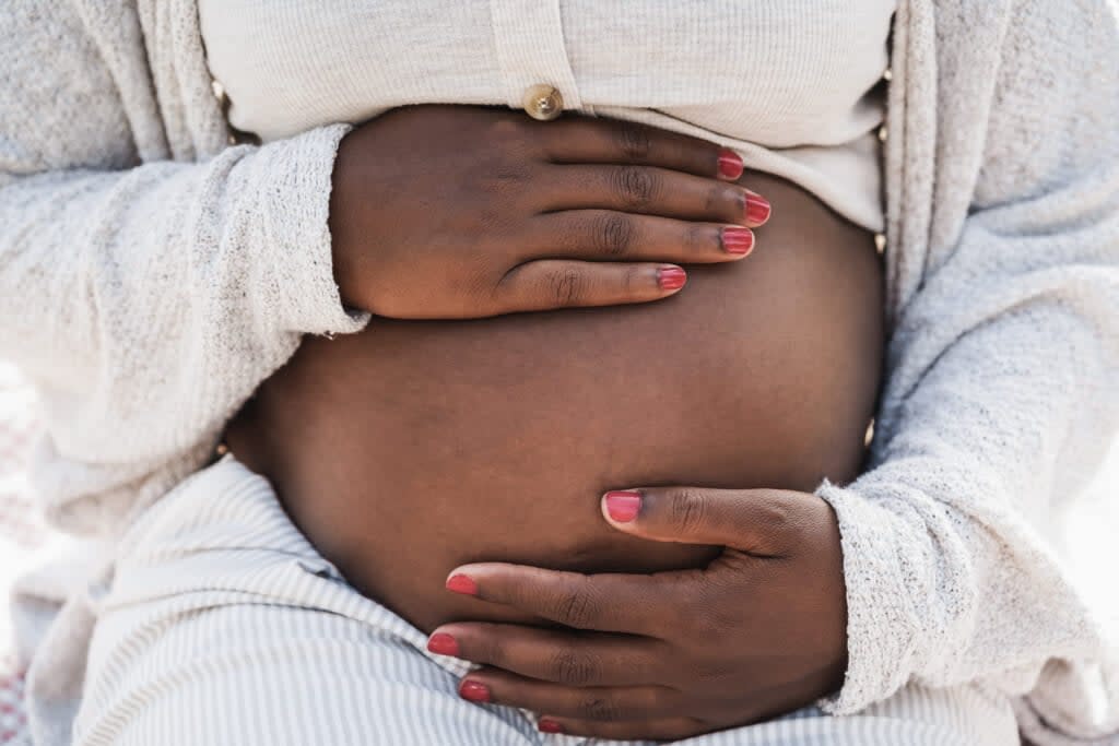 Close up of african pregnant woman holding her belly – Focus on hands