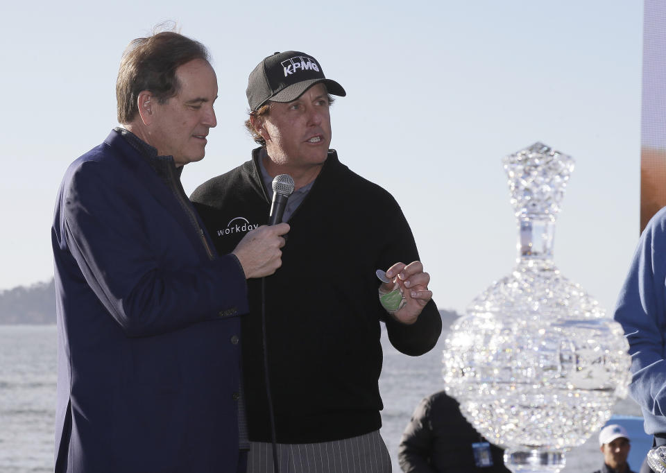 FILE - In this Monday, Feb. 11, 2019, file photo, while being interviewed by broadcaster Jim Nantz, left, Phil Mickelson holds up a silver dollar that belonged to his grandfather during an awards ceremony on the 18th green of the Pebble Beach Golf Links after winning the AT&T Pebble Beach Pro-Am golf tournament, in Pebble Beach, Calif. Nantz has worked the Final Four and Masters for the last 34 years and is missing them in 2020 because of the new coronavirus pandemic. (AP Photo/Eric Risberg, File)